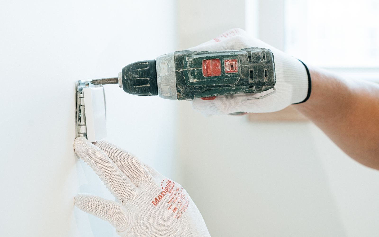 Handwerker installiert mit Bohrschrauber eine Steckdose an der Wand